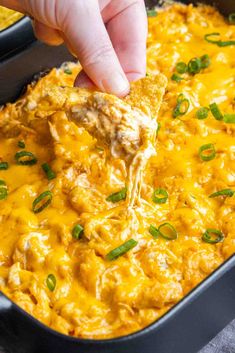 a hand dipping a tortilla chip into a casserole dish with cheese and green onions