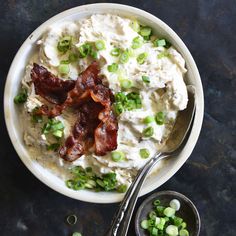 a bowl filled with mashed potatoes, bacon and green onions next to a spoon