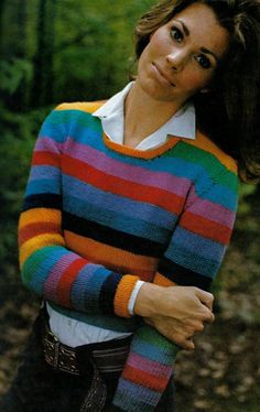 a woman wearing a colorful striped sweater posing for a photo in the woods with her hands on her hips