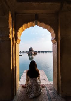 a woman sitting on a ledge looking out at the water