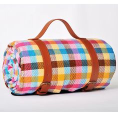 a multicolored plaid duffel bag sitting on top of a white table next to a brown leather handle