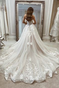 a woman standing in front of a mirror wearing a wedding dress with flowers on it