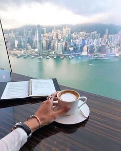 a person sitting at a table with a cup of coffee in front of the city