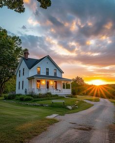 a white house sitting on top of a lush green field next to a forest at sunset