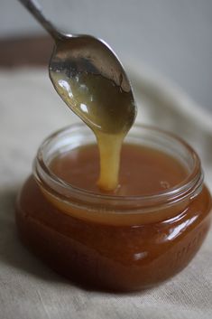 a spoon full of honey sitting on top of a glass jar filled with liquid and sauce