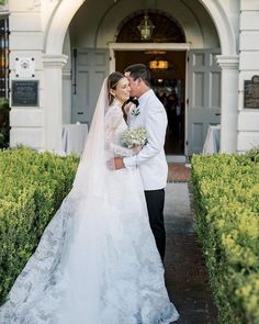 a bride and groom standing in front of an ornate white building with hedges on either side