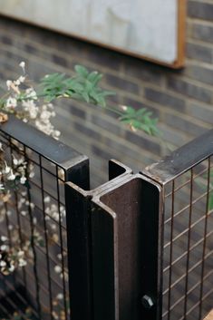 a metal fence with flowers growing out of it and behind it is a brick wall