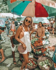 a woman standing under an umbrella next to baskets of fruit