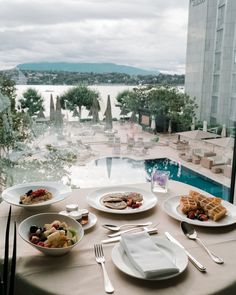 a table with plates and silverware on it near a swimming pool, overlooking the water