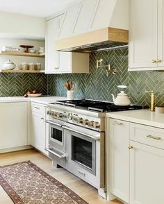 a kitchen with white cabinets and green tile backsplash, gold pulls on the range