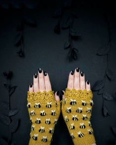 a woman's hands with black fingernails and yellow knitted mitts on them