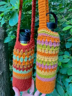 two crocheted water bottles in the shape of purses hanging from a tree