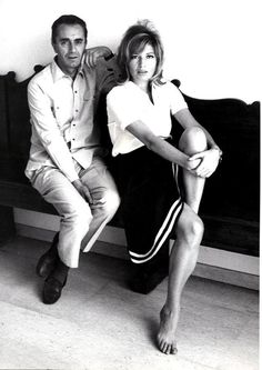 a man and woman sitting on a bench in black and white photo, posing for the camera