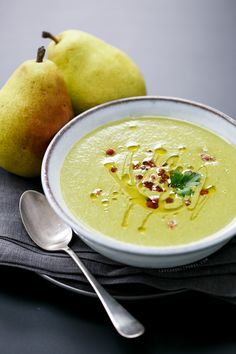 a bowl of soup next to two pears on a napkin with a spoon in it