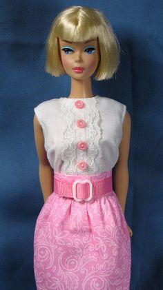 a barbie doll wearing a pink and white dress with buttons on the front, standing against a blue background