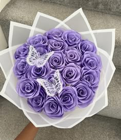 a bouquet of purple roses with two butterflies on them, sitting on some stairs in front of someone's hand