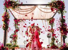 a newly married couple standing in front of an arch with flowers and petals on it