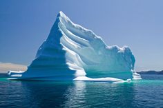 an iceberg floating in the middle of water with mountains and blue sky behind it