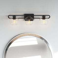 three lights on the wall above a mirror and a light fixture in front of a round mirror