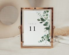 the table numbers are displayed in front of a white and gold frame with greenery