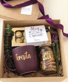 two coffee mugs in a gift box with purple ribbon and some flowers on the table