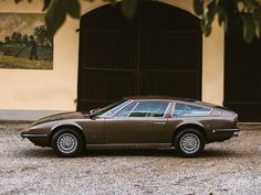 a brown sports car is parked in front of a building with two doors and windows