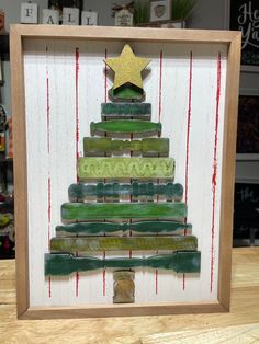 a christmas tree made out of popsicle sticks in a wooden frame on top of a table