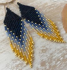 two tone beaded earrings with gold and blue beads hanging from a hook on a wooden table