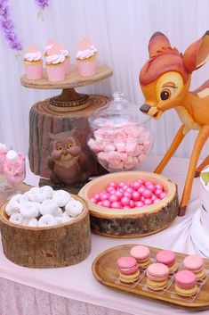 a table topped with cakes and desserts covered in frosted icing next to a deer statue