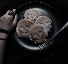 a person holding a fork and plate with three cookies decorated like skulls on top of it