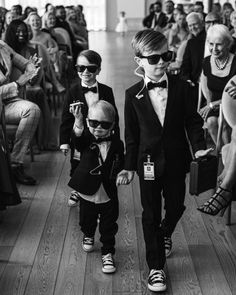 two young boys in tuxedos are walking down the aisle