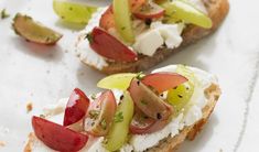 two pieces of bread with fruit and cheese on them sitting on a white tablecloth