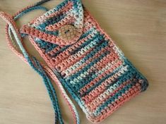 a crocheted purse sitting on top of a wooden table next to a cell phone