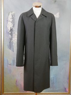 This charcoal gray overcoat is crafted from a high-quality wool-blend fabric, has a notch collar, and closes in the front with three concealed black buttons. The raglan style long sleeves feature a buttoned cuff strap, and the coat has two slanted storm pockets. The coat is lined in a black satin polyamid fabric (with one inner pocket), and a center vent in the back ensures complete ease of movement. Brand label: Oratop (Finland) Size: 44 US/UK Material: 45% Wool, 55% Polyester Condition: Near M Gray Outerwear With Concealed Placket For Work, Gray Business Outerwear With Suit Collar, Gray Wool Single-breasted Outerwear, Gray Wool Outerwear With Concealed Placket, Gray Business Wool Coat With Pockets, Classic Gray Wool Coat For Winter, Gray Wool Coat With Pockets For Business, Business Gray Wool Coat With Pockets, Gray Business Pea Coat With Button Closure