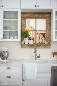 a kitchen sink sitting under a window next to a wooden shelf with flowers in it