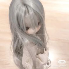 a doll with long gray hair standing on a wooden floor