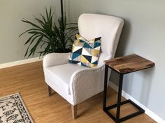 a chair with a pillow on it next to a small table and plant in the corner