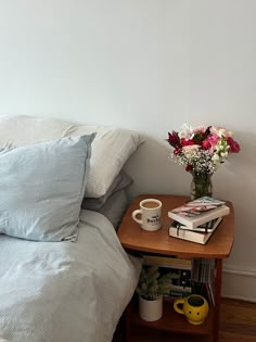 a bed with two pillows and a book on top of it next to a vase filled with flowers