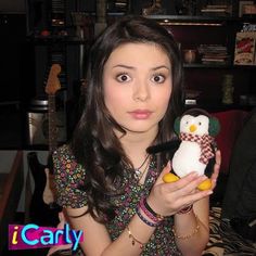 a girl holding a stuffed penguin toy in her right hand and looking at the camera