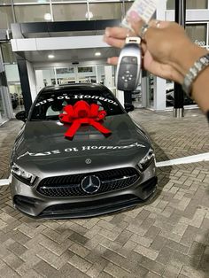 a person holding a cell phone in front of a car with a red bow on it