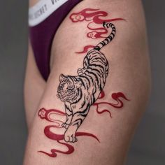 a woman's thigh with a tiger tattoo on the side and red flames coming out of it