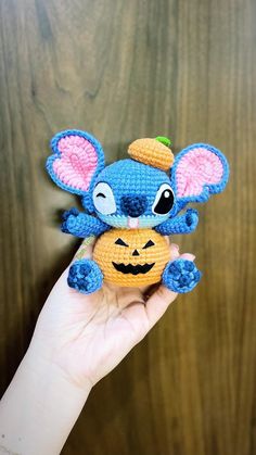 a hand holding a small crocheted mouse with a pumpkin in it's mouth