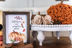 an arrangement of pumpkins and other fall decorations on a table with a framed sign