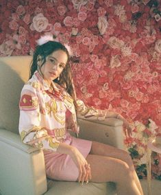 a woman sitting on top of a chair in front of a flower wall with roses