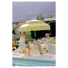 three women sitting under an umbrella next to a pool