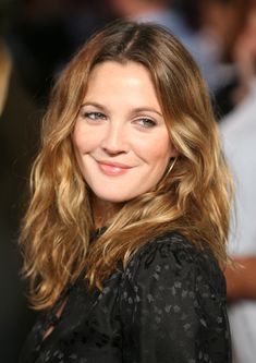 a close up of a person wearing a black shirt and smiling at the camera with people in the background