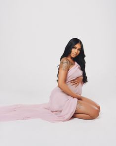 a pregnant woman sitting on the floor in a pink dress with her hands on her stomach