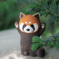 a red panda bear figurine sitting next to a pine tree