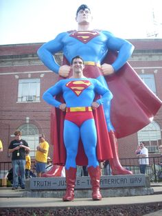 a man standing next to a giant superman statue