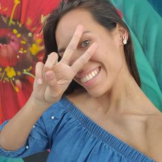 a woman is making the peace sign with her hand and smiling at the camera while standing in front of an umbrella